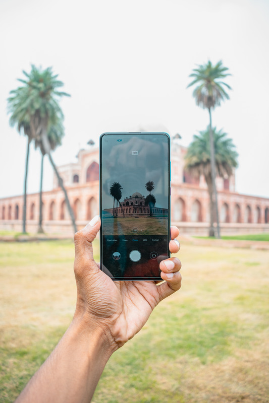 make money with photography as a beginner - male hand holding up a smartphone taking a photo of a building and palm trees.